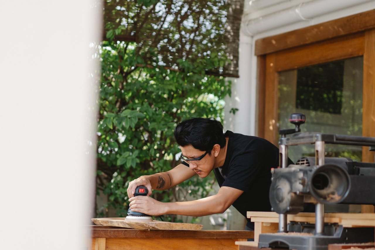 A skilled craftsman using a sander on wood in an outdoor workshop.